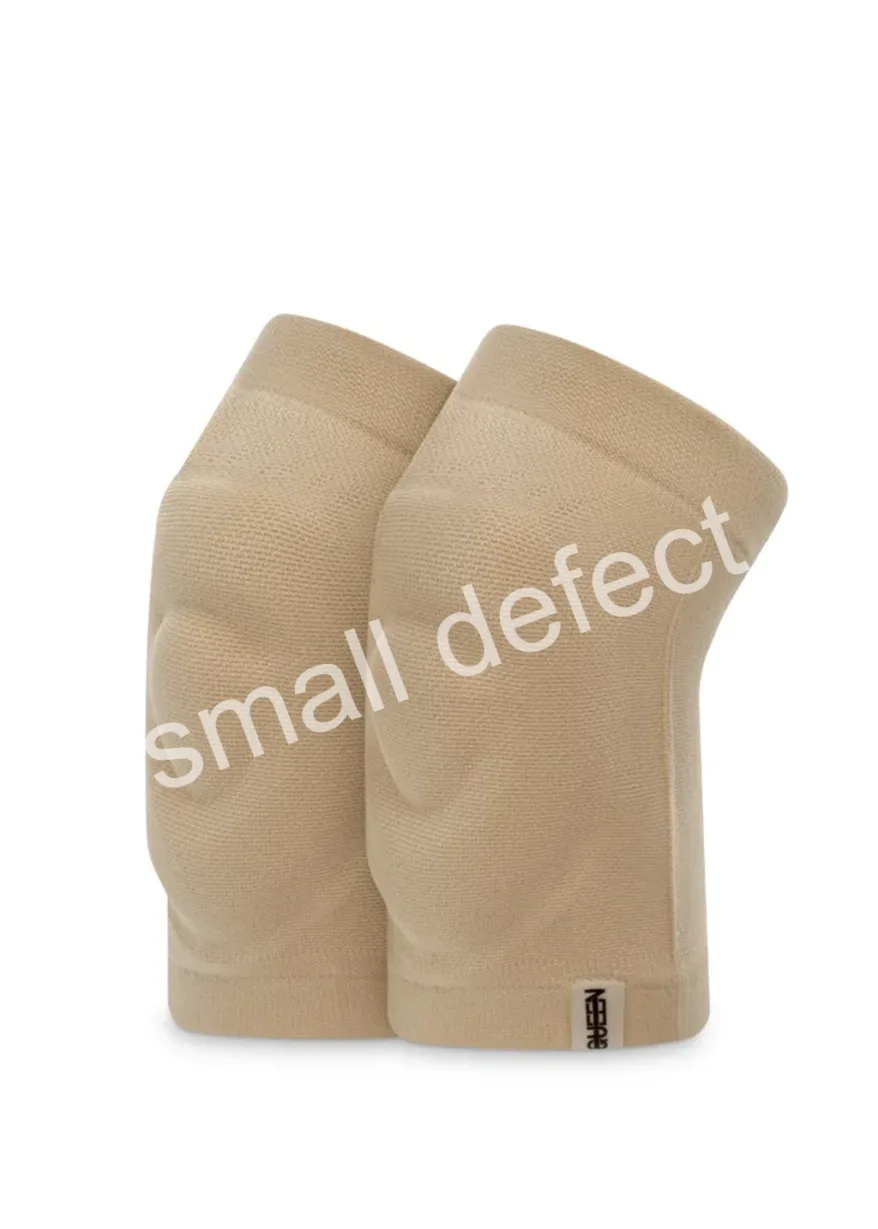 Beige pair of knee sleeves standing upright with textured fabric and a small tag at the bottom edge.