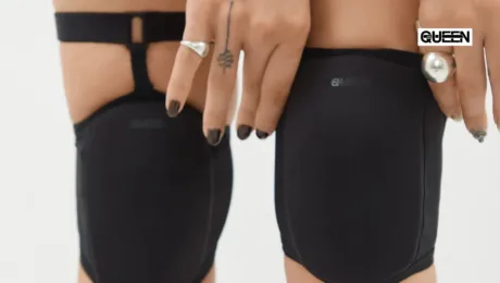 Back view of two people wearing black athletic shorts; a 'QUEEN' logo is visible on the right short edge.