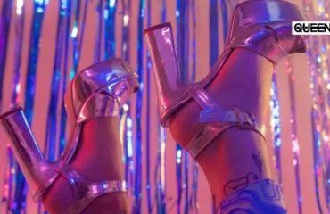 How to Dance in Heels Tips for Your First Heels Class Close-up of shiny pink metallic high-heeled sandals on a leg, neon backdrop, with a tattoo visible on the ankle.
