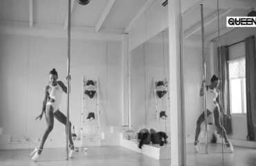 Is Pole Dancing Hard What to Really Expect as a Beginner Pole dancer in a white leotard practicing a move beside a vertical pole in a mirrored dance studio.